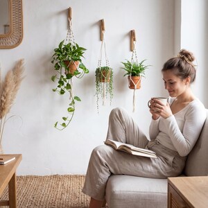 A woman sits comfortably on a couch, reading a book and sipping a beverage, surrounded by potted plants and a woven basket, creating a cozy and relaxing atmosphere.