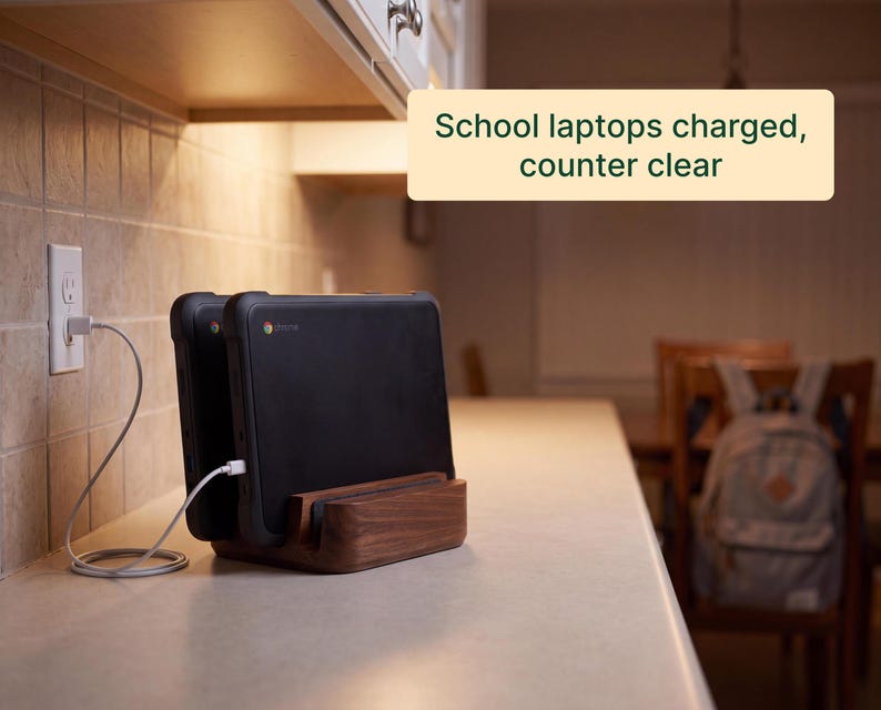 A kitchen counter with two school laptops charging, and a wooden charging dock holding the laptops.