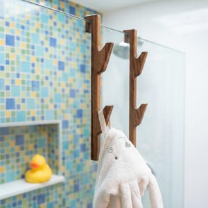 A white towel with a face on it is hanging from a wooden towel rack in a bathroom with a colorful tiled wall.