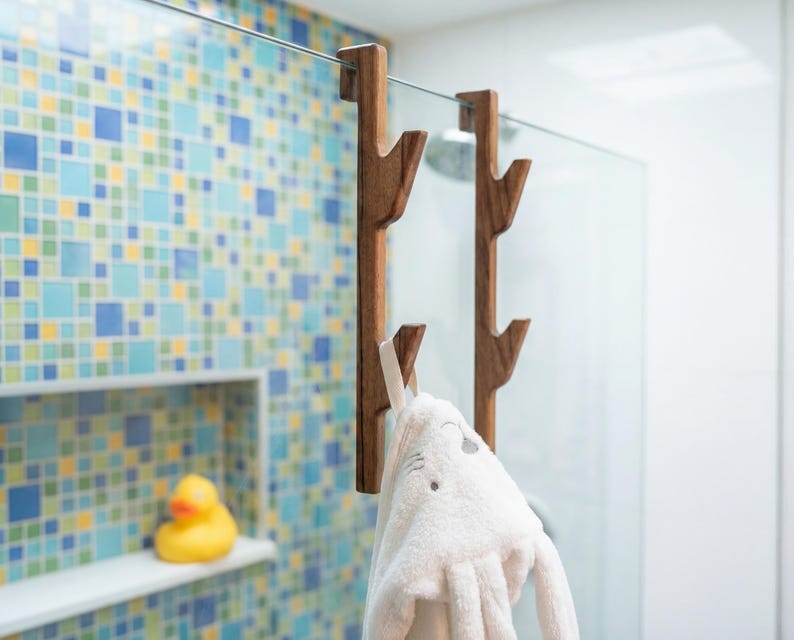 A white towel with a face on it is hanging from a wooden towel rack in a bathroom with a colorful tiled wall.