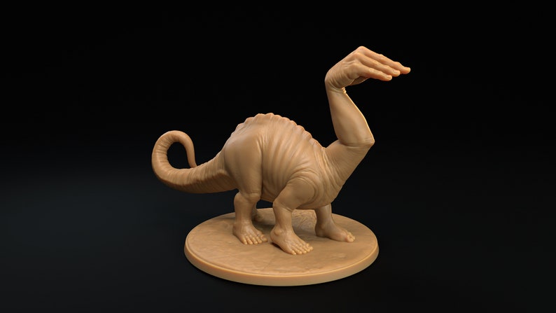 Op de afbeelding: Een bruin, gebeeldhouwd beeldje van een dinosaurus met een menselijke arm als nek. De dinosaurus staat op een ronde basis.