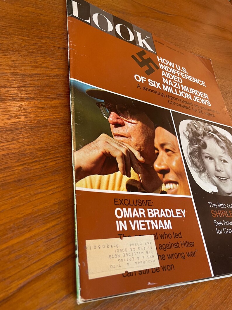 May include: A vintage LOOK magazine cover featuring a brown background with white and black text. The cover displays a swastika, a photograph of two men, and a portrait of a young girl. A white mailing label is affixed to the lower section.