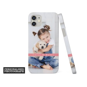 Op de afbeelding: Witte iPhone-hoes met een foto van een jong meisje dat een golden retriever puppy knuffelt. De hoes heeft een roze streep met de tekst "Chloe & Buddy". De woorden "Personalised Photograph" staan in een zwarte doos.