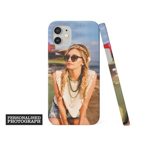 Op de afbeelding: Een gepersonaliseerde telefoonhoes met een foto van een vrouw met een zonnebril en een witte top, leunend tegen een vintage groene auto. De hoes heeft een lichtblauwe lucht als achtergrond. De tekst "PERSONALISED PHOTOGRAPH" is afgedrukt.