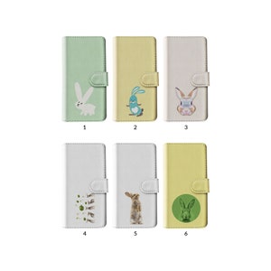 May include: Six phone cases in pastel shades of green, yellow, and white, each featuring a different rabbit design. The cases have a flip-style design with a magnetic clasp. The bunny illustrations range from cartoonish to realistic.