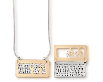 May include: A gold and silver necklace with a sliding pendant. The pendant has a cutout of a tree and the words "If it hurts too much to look back, but you're too scared to look ahead, just look beside you and I'll be there." on one side and "To look back, you're too scared to look ahead, just look beside you and I'll be there." on the other side.