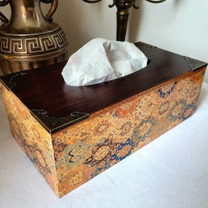 Op de afbeelding: Een houten tissuebox-hoes met een decoratief bloemenpatroon in tinten oranje, blauw en groen. De hoes heeft een messing rand en een rechthoekige vorm.