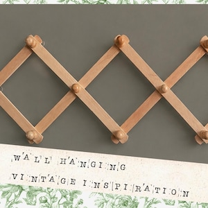 May include: A light brown wooden wall-mounted coat rack with a diamond-shaped design. The rack has multiple wooden pegs for hanging items. The text "WALL HANGING VINTAGE INSPIRATION" is at the bottom.