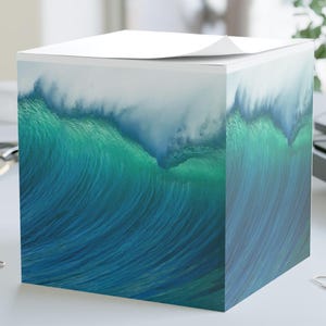 May include: A square memo cube featuring a printed graphic of a large, curling ocean wave. The design displays deep blue and vibrant turquoise water tones transitioning into white sea foam at the top edge of the paper stack, creating a continuous image.