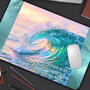 May include: A rectangular desk mat featuring a vibrant ocean wave graphic with teal, blue, and sunset-hued water. The text reads: Jeremiah 31:35 He Who Stirs Up the Sea the Lord Almighty Is His Name. The mat has a black border and rounded corners.