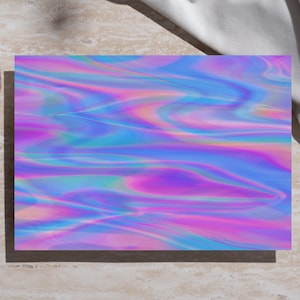 May include: A rectangular art print with a vibrant, iridescent design in shades of pink, purple, and blue. The print is placed on a light-colored surface, with a glass of tea and a white cloth in the background.