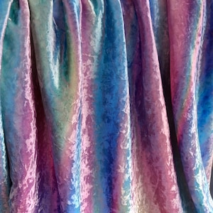 May include: A draped fabric with a shimmering, iridescent effect. The material features a blend of colors, including shades of blue, pink, purple, and green. The fabric's texture appears soft and velvety, with subtle variations in color across its surface.