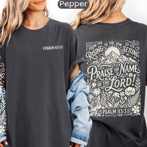 May include: Dark gray t-shirt with the text "Psalm 113:3" on the front. The back of the shirt features a mountain scene with the words "Praise the Name of the Lord!" and "From the rising of the sun to its setting."
