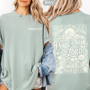 May include: A light green t-shirt with the text "PSALM 113:3" on the front. The back of the shirt features a mountain and floral design with the words "PRAISE THE NAME OF THE LORD!" and "PSALM 113:3".