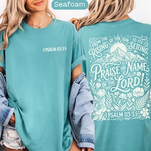 May include: Seafoam-colored t-shirt with the text "PSALM 113:3" on the front. The back of the shirt features a mountain and floral design with the words "FROM THE RISING OF THE SUN TO ITS SETTING, PRAISE THE NAME OF THE LORD!" and "PSALM 113:3".