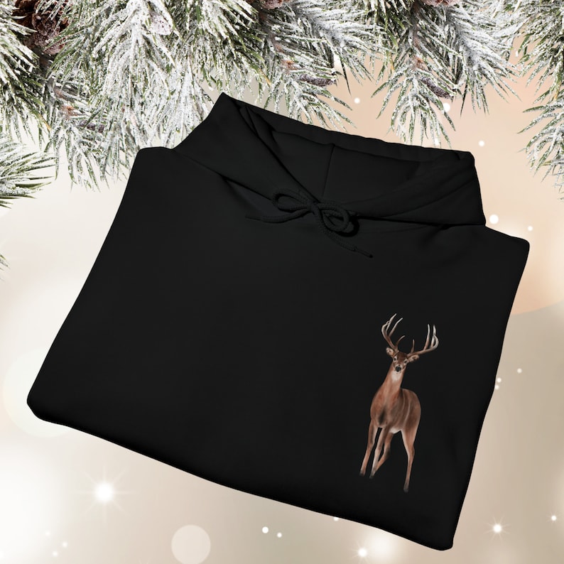 May include: A black hooded sweatshirt featuring a graphic of a brown deer with antlers positioned on the lower right side. The garment includes a hood with matching black drawstrings and long sleeves, presented in a folded, flat-lay orientation.