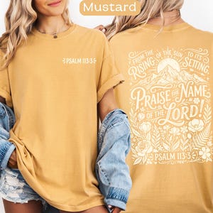 May include: Mustard-colored t-shirt with the text "PSALM 113:3" on the front. The back of the shirt features the phrase "PRAISE THE NAME OF THE LORD!" with floral and mountain illustrations. The text "FROM THE RISING OF THE SUN TO ITS SETTING" is also included.