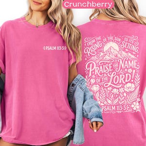 May include: A vibrant pink t-shirt with rolled-up sleeves. The front features the text "PSALM 113:3" in white. The back displays a detailed graphic with the words "Praise the Name of the Lord!" and "From the rising of the sun to its setting," along with floral elements.