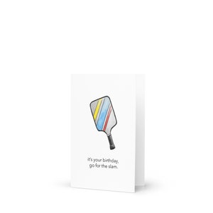 May include: White birthday card featuring a watercolor illustration of a pickleball paddle with yellow, blue, and red stripes. The card reads "it's your birthday, go for the slam."