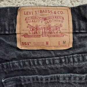 May include: A pair of black denim jeans featuring a tan leather patch on the back waistband. The patch displays the Levi Strauss & Co. logo, two horses pulling jeans, and the text 551 Relaxed Fit Tapered Leg with blank spaces for W and L.