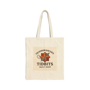May include: Cream-colored tote bag with the text "TECHNOMANCER'S TIDBITS QUILT SHOP" in a brown and orange logo. The logo features a needle and thread through a geometric star design. The bag has two handles.