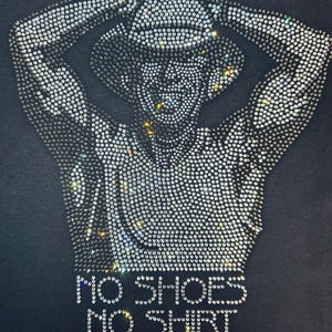 May include: Black t-shirt featuring a rhinestone design of a person with arms raised, wearing a cowboy hat. The text "NO SHOES NO SHIRT NO PROBLEMS" is spelled out in rhinestones below the image.