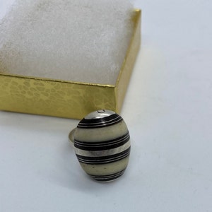 May include: A silver ring with a white and black striped oval stone. The stone has a silver band around it.
