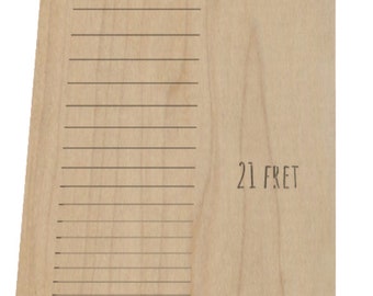 May include: A light-colored wooden guitar fretboard with etched lines and the text "21 FRET". The fretboard has a natural wood grain pattern and is angled slightly.