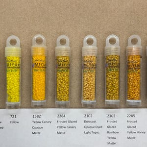 以下が含まれることがあります： 黄色、オレンジ、茶色の様々な色合いのミユキ デリカ ビーズが入った小さなボトルが10本あります。各ボトルには、番号と色の説明が付けられています。例えば、「薄い黄色セイロン裏地染め」、「黄色カナリア不透明マット」、「フロストガラスイエローカナリアマット」などです。