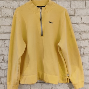 May include: A yellow quarter-zip sweatshirt with a black Reebok logo on the left chest. The sweatshirt has a ribbed collar and cuffs.