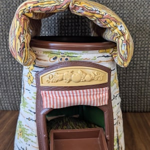 May include: A vintage toy shop with a brown plastic facade, a red and white striped awning, and a small brown tray. The shop is decorated with a fabric roof and walls with a colorful pattern. A brown plastic train sits on top.