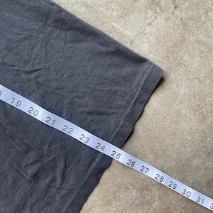 May include: Close-up of a dark gray t-shirt with a measuring tape laid across it. The tape shows measurements from 19 to 31 inches. The fabric has a slightly worn appearance.