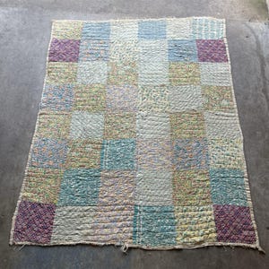 May include: A patchwork quilt with a grid pattern of various fabrics in pastel colors. The quilt features squares of floral prints, stripes, and solid colors, including blue, green, purple, and cream. The quilt is likely vintage or handmade.