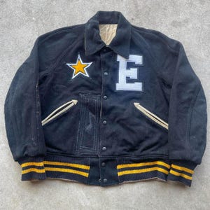 Peut inclure: Veste de style universitaire noire avec une étoile jaune et la lettre "E" sur le devant. La veste a des poignets rayés jaunes et noirs et un col beige. Comprend un écusson de note de musique.