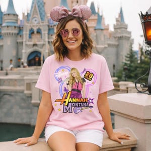 K&ouml;nnte beinhalten: Ein hellrosa T-Shirt mit einer Grafik von Hannah Montana, dem Text "Hannah Montana" und "20 Years". Das Shirt hat ein Disney-Logo und Noten. Die Person tr&auml;gt eine rosa Schleife und eine Sonnenbrille.