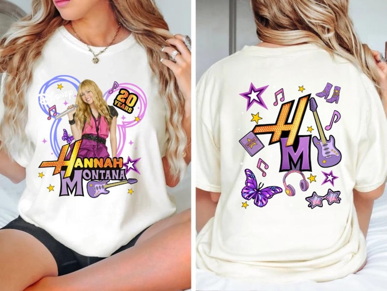 K&ouml;nnte beinhalten: Cremefarbenes T-Shirt mit einem Hannah Montana-Grafik und dem Text "20 Years". Das Frontdesign umfasst eine lila Gitarre, Schmetterlinge und Sterne. Die R&uuml;ckseite hat ein lila "HM"-Logo mit Noten, Sternen und anderen Grafiken.