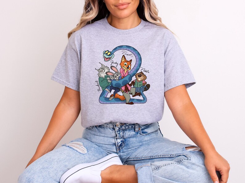 Puede incluir: Camiseta gris claro con un dibujo animado colorido de personajes de una pel&iacute;cula. El dibujo incluye un n&uacute;mero 2 azul, un zorro, un conejo, un castor y un gato. Los nombres de los personajes est&aacute;n escritos encima.