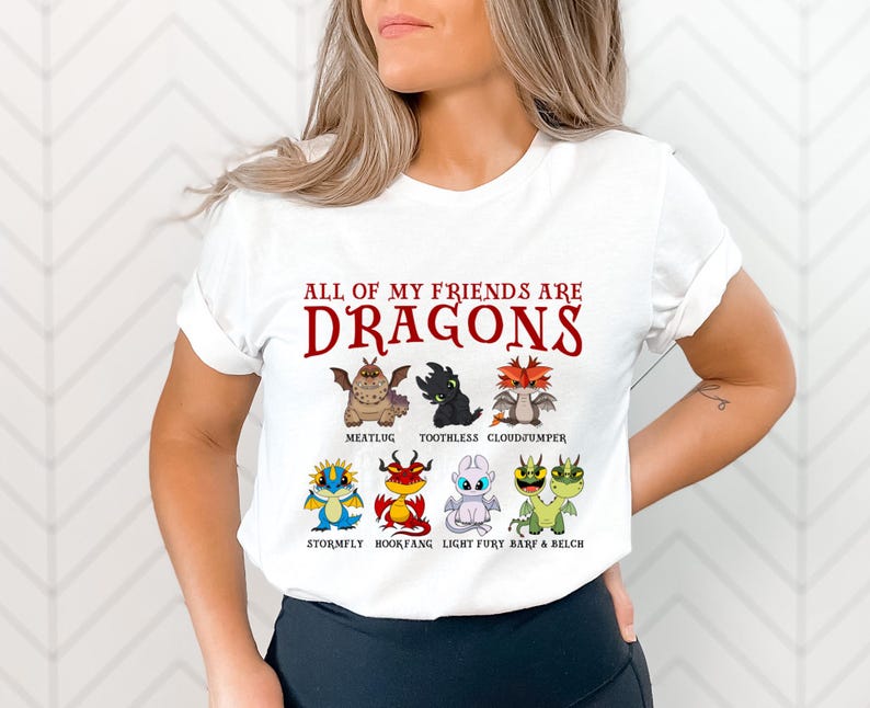 May include: White t-shirt with the text "All of my friends are dragons" in red. The shirt features a cartoon illustration of eight dragons, including Toothless, Meatlug, Cloudjumper, Stormfly, Bookfang, Light Fury, Barf, and Belch.