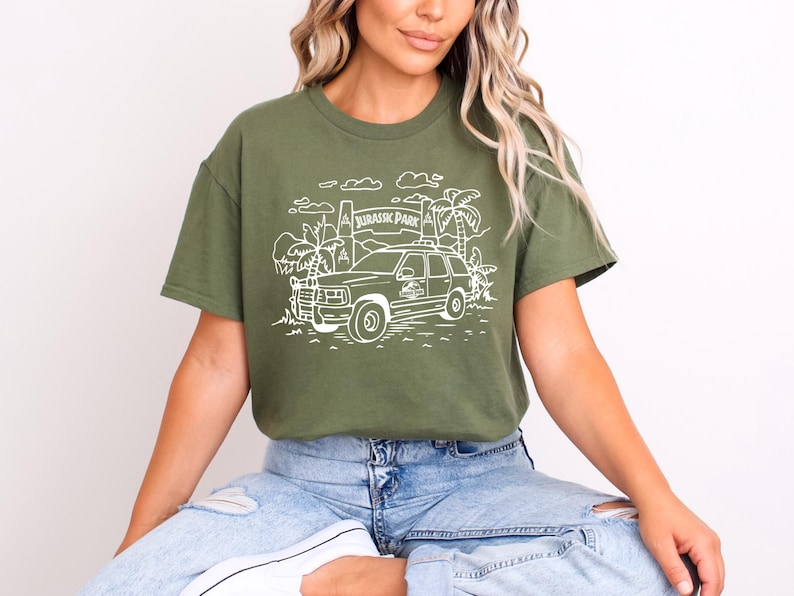 May include: A green t-shirt with a white graphic of a jeep driving through a jungle with the text "Jurassic Park" on a sign.