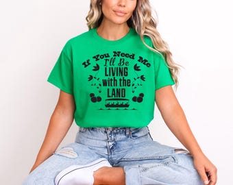 May include: A green t-shirt with a black graphic that says "If You Need Me I'll Be Living With The Land". The graphic also includes a boat and flowers.