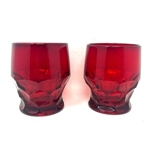 May include: Two red glass tumblers with a faceted design. The glasses are empty and have a clear, shiny finish.