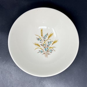 May include: A white ceramic bowl with a floral design featuring blue flowers and wheat stalks in brown and yellow.