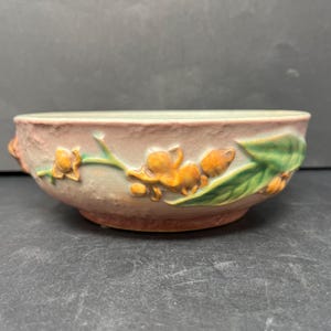 May include: A vintage ceramic bowl with a floral design. The bowl is decorated with yellow flowers and green leaves on a pink background.