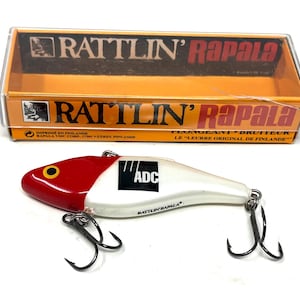 May include: A white and red fishing lure with a black and white logo that says "ADC" and the text "RATTLIN' RAPALA". The lure has three treble hooks.