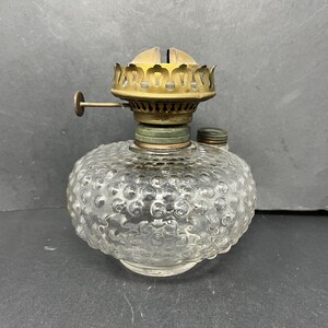 May include: A clear glass oil lamp with a textured, bubbled surface. The lamp has a gold metal top with a decorative design.