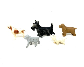 May include: A collection of five small dog figurines in various breeds and colors. Includes a black Scottish Terrier, a brown Cocker Spaniel, a white and brown spotted dog, a light gray bulldog, and a cream-colored dog.