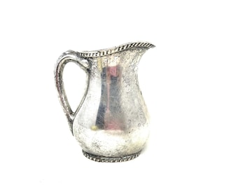 May include: A silver pitcher with a textured surface and a rounded body. The pitcher has a handle and a spout.