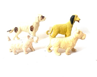 May include: Four small dog figurines in various poses. Two are off-white with brown spots, one is yellow with black ears, and the last is off-white with a textured coat. The dogs are on a white background.