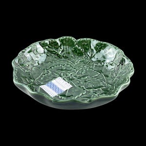 Peut inclure: Un saladier vert en céramique en forme de feuille. Le bol présente un motif de feuilles détaillé et une finition brillante. Une petite étiquette avec un motif bleu et blanc est attachée au bol.