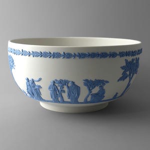 May include: A white ceramic bowl featuring a matte finish with raised blue relief decorations. The exterior displays a continuous band of blue laurel leaves at the rim and a series of blue figures and trees encircling the body of the bowl.